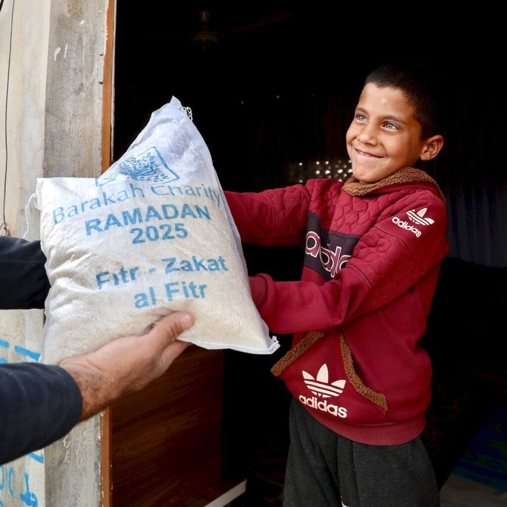 A smiling boy receiving a bag of rice marked for Zakat al-Fitr distribution during Ramadan.