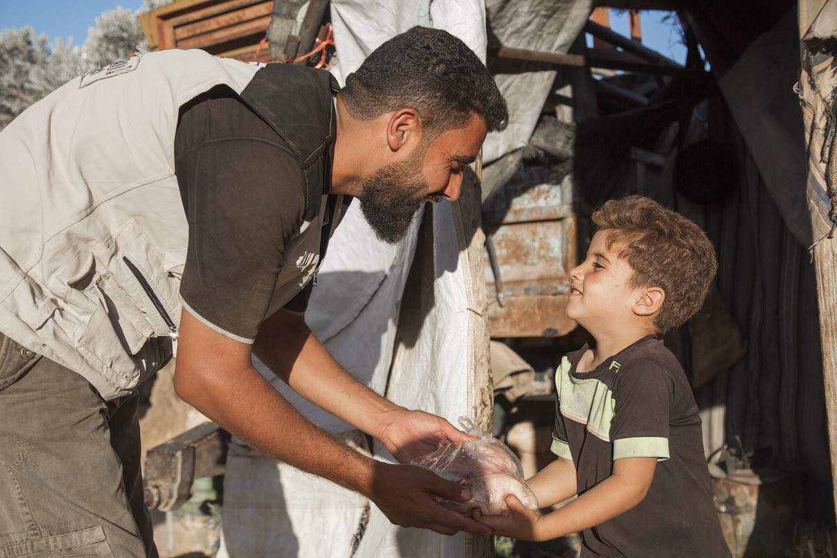 An aid worker giving qurbani food to a boy.